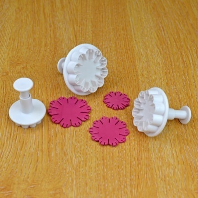 Conjunto de cortadores de plástico branco para modelagem com recortes florais rosas sobre madeira.