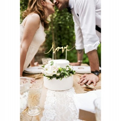 Bolo branco decorado com flores e topo dourado com a palavra love numa mesa ao ar livre