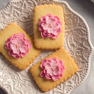 Três bolachas retangulares com flores rosas de pasta de açúcar no prato branco decorado.