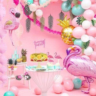 Decoração de festa tropical com balões, flamingos e bolo com frutas.