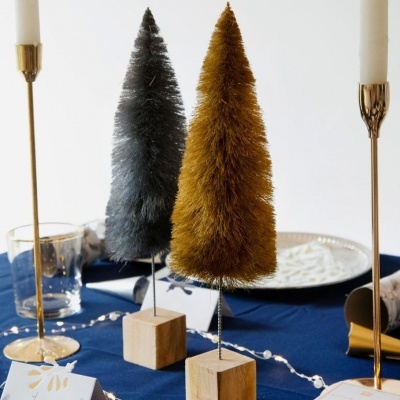 Dois pinheiros decorativos em cinza e dourado com base de madeira numa mesa decorada