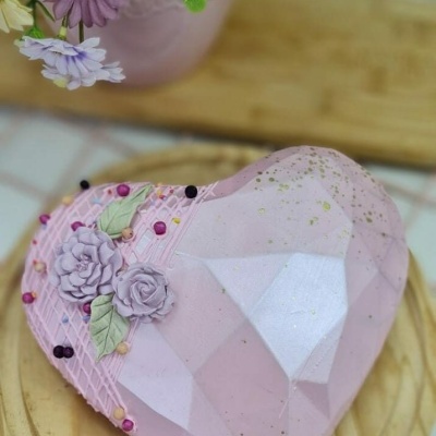 Sobremesa em forma de coração rosa claro com decoração floral e pérolas sobre base de madeira.