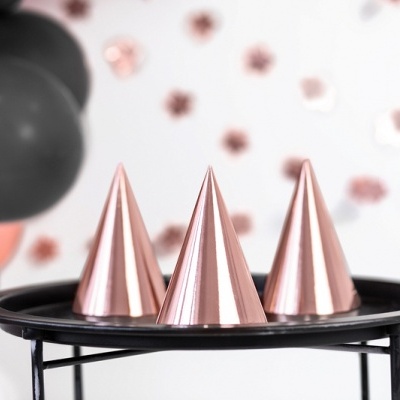 Três chapéus metálicos rosas em tabuleiro preto com balões ao fundo