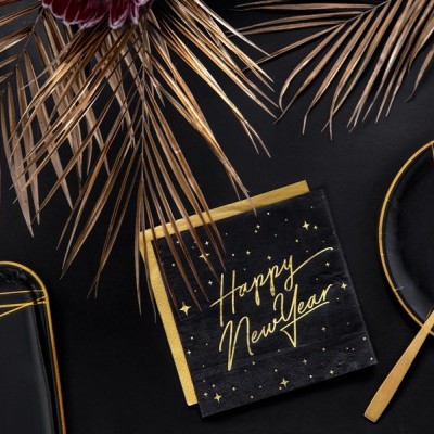 Guardanapo preto com texto dourado 'Happy New Year' sobre mesa preta com decoração dourada