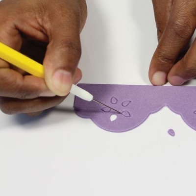 Mãos a cortar padrão em papel roxo com ferramenta amarela