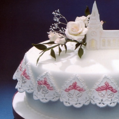 Bolo branco com decoração floral e figura de igreja