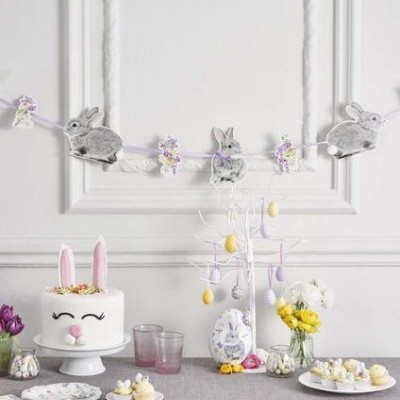 Decoração de Páscoa com bolo de coelho, guirlanda de coelhinhos, arranjos de flores e ovos decorativos sobre mesa