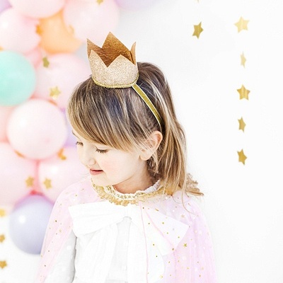Criança com coroa dourada e capa rosa com estrelas douradas em fundo festivo