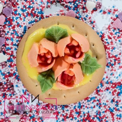 Biscoito decorado com flores de creme rosa e folhas verdes, sobre confeitos coloridos