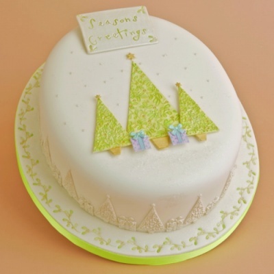 Bolo de Natal redondo com decoração de árvores verdes e texto Seasons Greetings