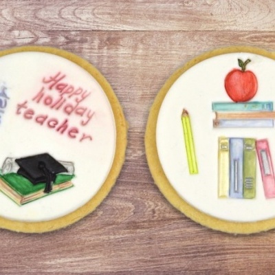 Dois biscoitos decorados com glacê branco e desenhos relacionados à escola em madeira.