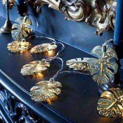 Cordão de luzes com folhas douradas Monstera sobre móvel de madeira escura esculpida