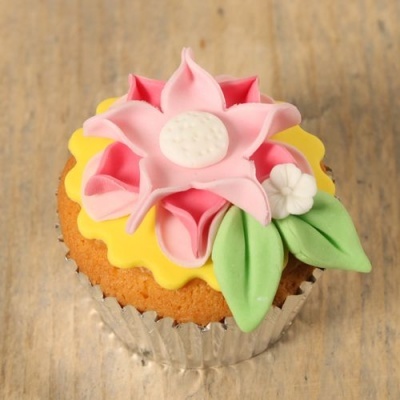 Cupcake decorado com glacê em forma de flor rosa com folhas verdes sobre base amarela ondulada