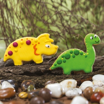 Biscoitos decorados em forma de dinossauros amarelo e verde sobre tronco com pedras