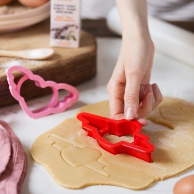 Cortador de biscoitos vermelho em formato de pássaro com coração em massa de biscoito na bancada de cozinha.