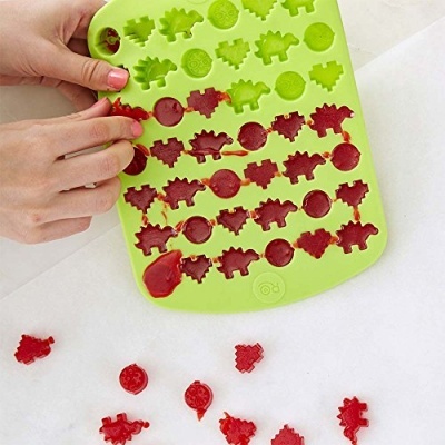 Forma de silicone verde com doces vermelhos em formatos de dinossauros e moedas.