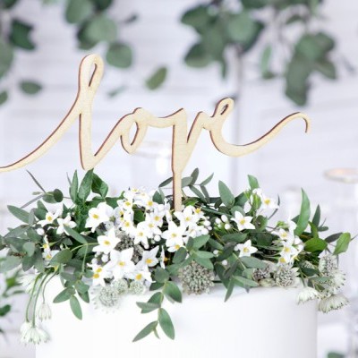 Topo de bolo dourado com a palavra love e decoração de flores brancas e folhas verdes