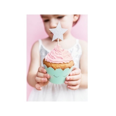 Cupcake com cobertura rosa e decoração de estrela, segurado por criança com vestido branco e fundo rosa