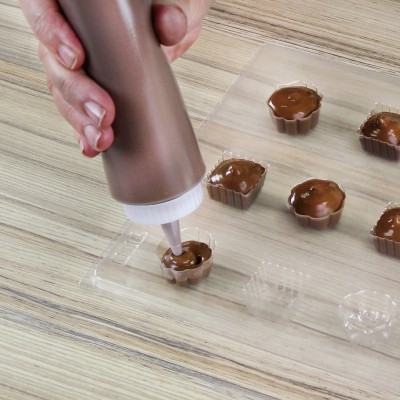 Moldes de bombons transparentes sendo preenchidos com chocolate castanho líquido