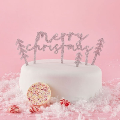Bolo branco com decoração prateada 'merry christmas' e pinheiros, açúcar em pó e doces em fundo rosa