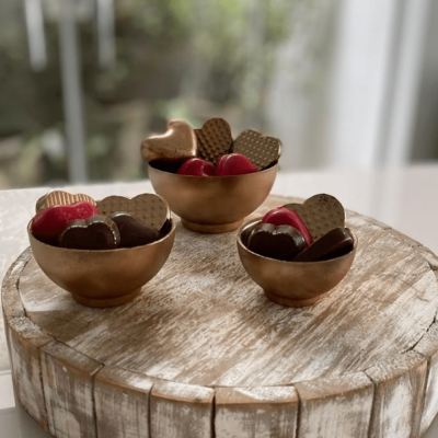 Três taças castanho claro com corações de chocolate coloridos sobre suporte de madeira rústica