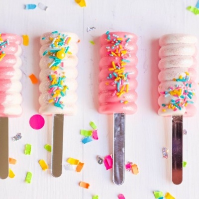 Quatro gelados em pau rosa e branco com granulados coloridos sobre fundo branco com confetes.