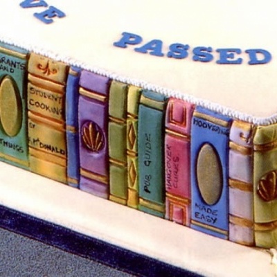 Bolo decorado que parece uma pilha de livros com títulos visíveis e texto em azul no topo