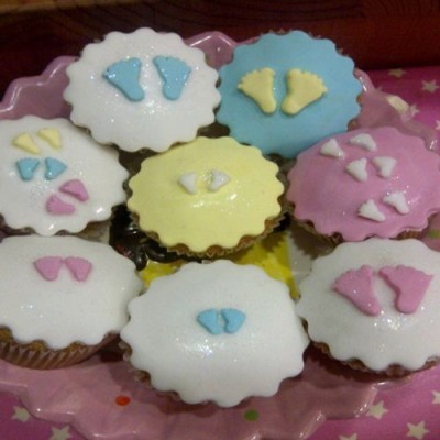 Oito cupcakes coloridos com glacê e pegadas decorativas num prato rosa