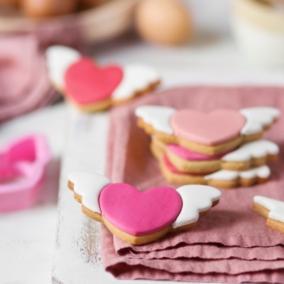 Bolachas em forma de coração com asas cor-de-rosa e branco sobre pano rosa e tábua branca