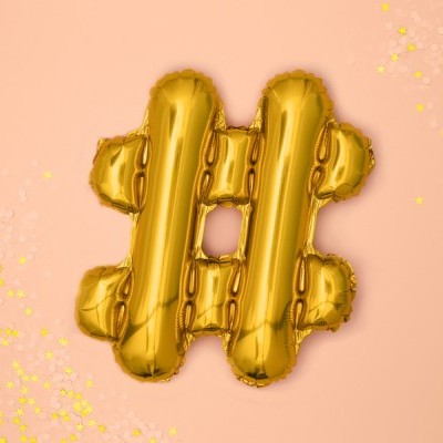 Balão metálico dourado em forma de hashtag num fundo rosa com confetes