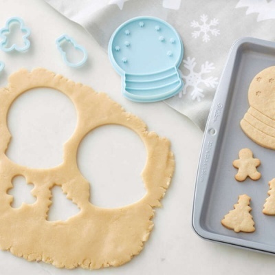 Conjunto de cortadores de biscoitos natalícios em plástico azul com massa e biscoitos em tabuleiro