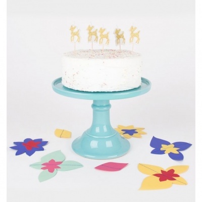 Bolo branco com velas douradas em forma de rena num suporte azul celeste, com recortes de papel coloridos à volta