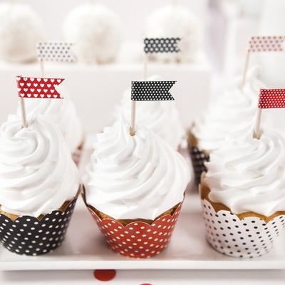 Seis cupcakes com cobertura branca e bandeirinhas coloridas em embalagem de bolinhas