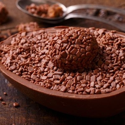 Ovo de Páscoa de chocolate ao leite com granulados de chocolate escuro em cima, colocado sobre mesa de madeira