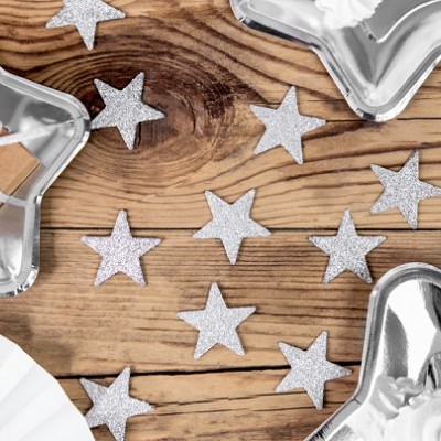 Pratos prateados em forma de estrela com decoração de estrelas pequenas prateadas e fundo de madeira