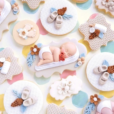 Biscoitos decorados com tema de bebé em tons pastel sobre superfície colorida