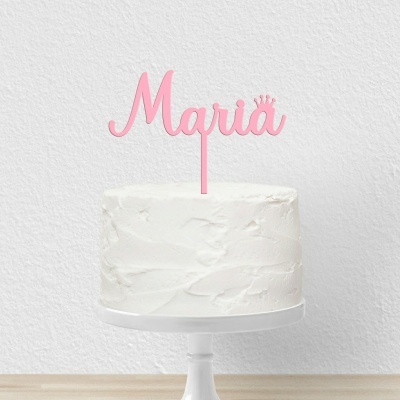 Bolo branco com topper rosa com o nome Maria em estilo cursivo e coroa, sobre suporte branco