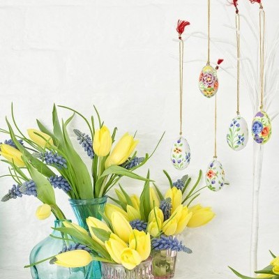 vasos de vidro com flores amarelas e azuis e galho decorativo com ovos de Páscoa suspensos