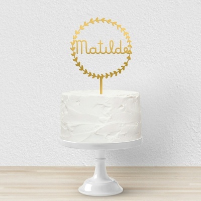 Bolo branco simples com topo de bolo dourado escrito Matilde em coroa de folhas