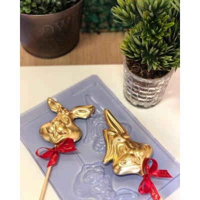 Pirulitos dourados em forma de coelhos com laços vermelhos junto a plantas em vaso sobre mesa