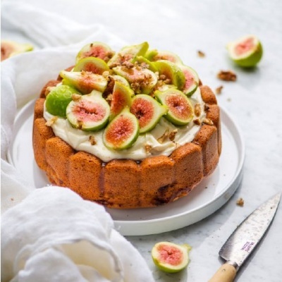 Bolo com cobertura de creme, figos cortados e nozes num prato branco