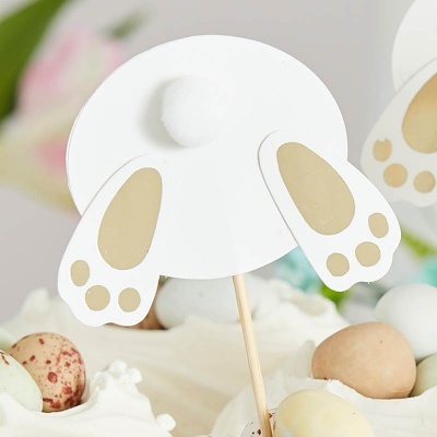 Decoração de bolo em forma de rabo e patas de coelho branco com detalhes dourados sobre creme e ovos decorativos