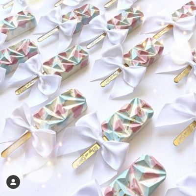 Gelados em pau com padrão geométrico e laços brancos organizados.