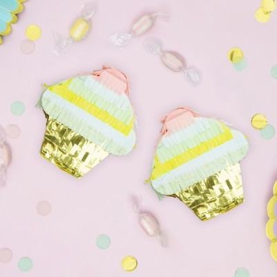 Dois piñatas de cupcake coloridos sobre superfície rosa com confetes e doces