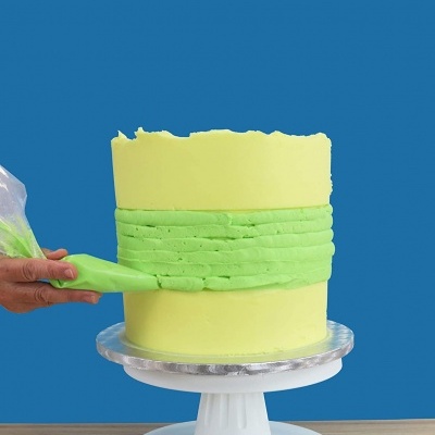 Bolo cilíndrico amarelo com faixa verde sendo decorado