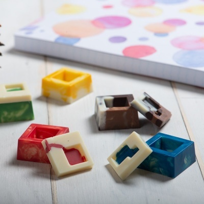 Bases e tampas de resina colorida quadradas em madeira clara com caderno ao fundo