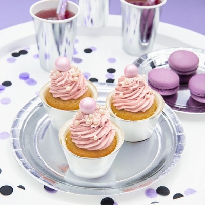 Cupcakes cor-de-rosa com macarons e copos prateados sobre mesa branca com confetis roxos