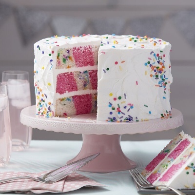 Bolo branco com granulados coloridos e interior rosa em suporte rosa claro