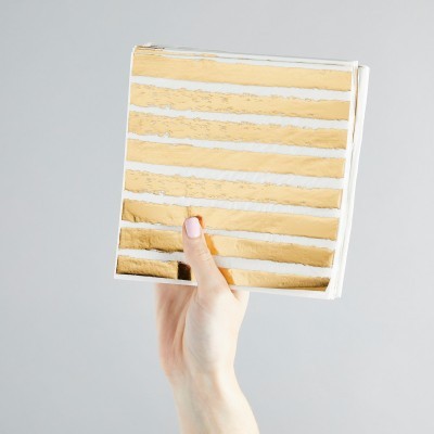 Guardanapos de papel brancos com riscas douradas metálicas segurados por uma mão