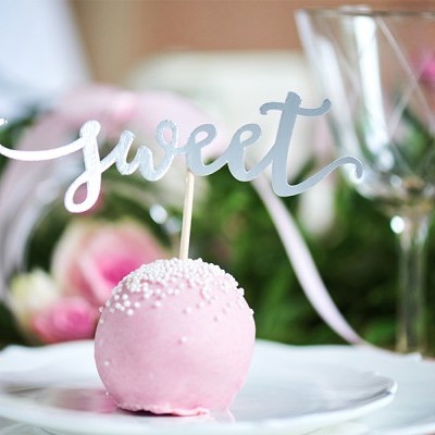 Doce rosa com cobertura de pérolas brancas e placa com a palavra 'sweet' num prato branco.